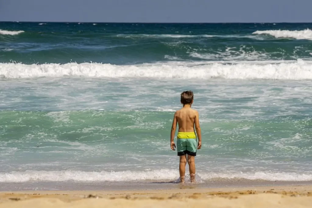 School aged boy standing on the beach about to go swimming on vacation.