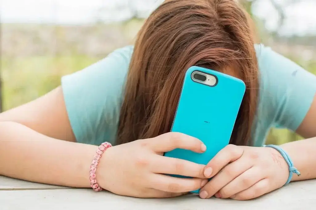 A teen hiding behind their smart phone.