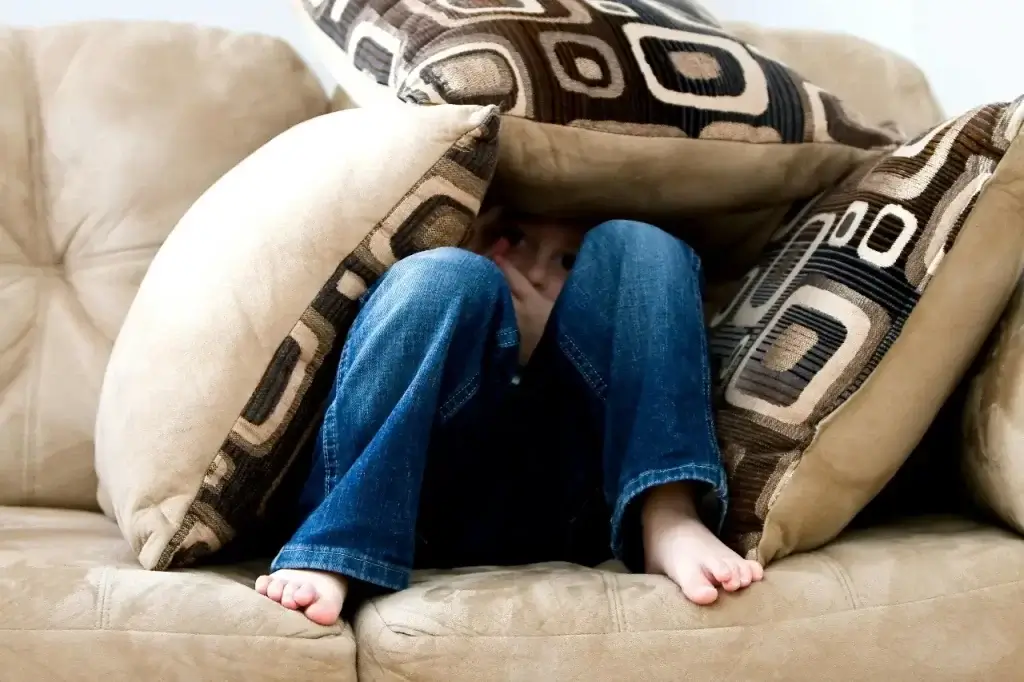 A child hiding in cushions because they feel homesick.