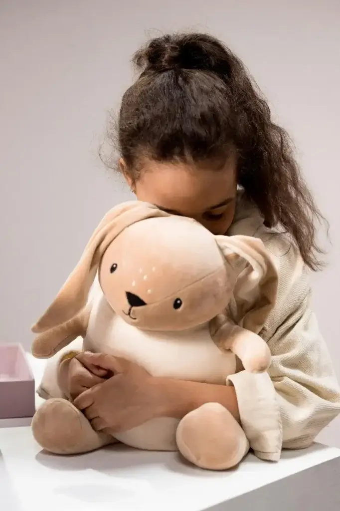 Child cuddling her toy, an important comfort item for her after her family has relocated abroad.