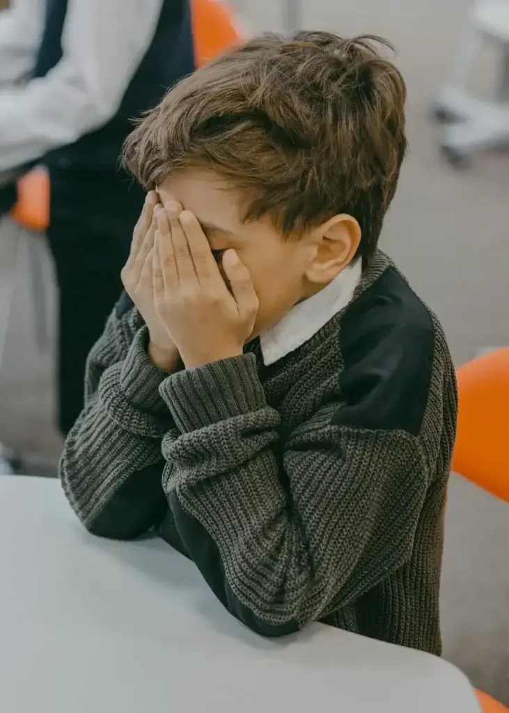 A young boy with his face in his hands as he processes the big move abroad.
