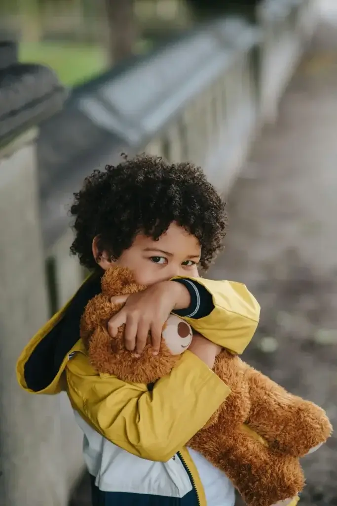 Child cuddling his teddy bear, acting out his need for familiarity after moving internationally with his family.