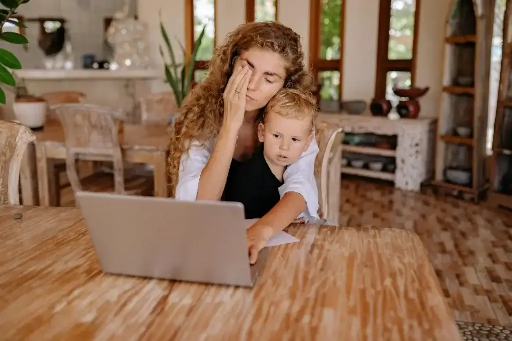 A Mother sitting with her child on her lap, looking at her computer, exhausted after her international relocation with children.