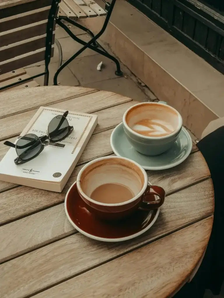 Two coffees on a table, half drunk, showing a Mother who has recently relocated abroad sharing a moment of relaxing with a friend. Something that helps the transition process flow smoothly.
